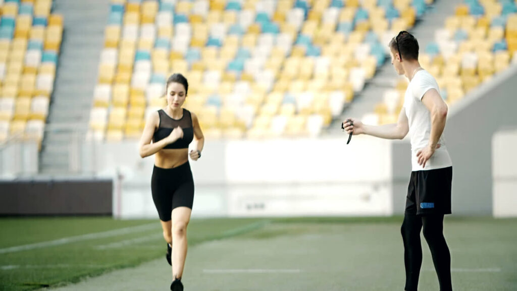 A woman jogs past while a Physiotherapist times her stride with a stopwatch