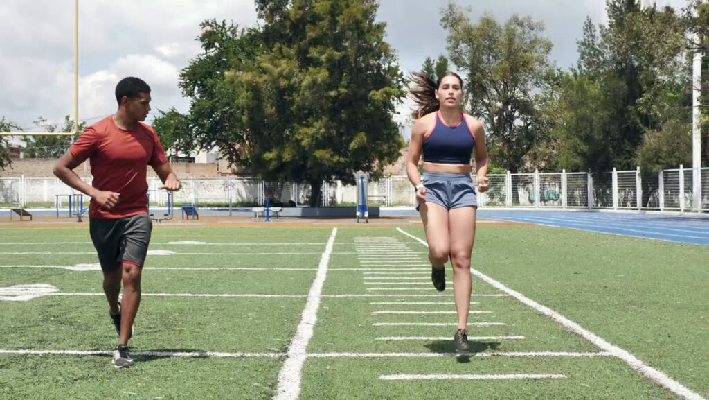 A Physiotherapist runs alongside a patient on a sports field during a return-to-running session
